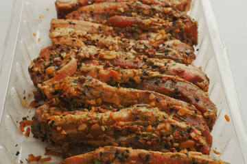 Fresh pork belly slices in Korean style marinate and herbs on a plastic tray on simple table cloth. Close up.