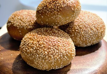 Ruddy rye homemade buns with sesame seeds on a flat wooden plate, bathed in beams of bright sun (on objects on the sides the focus is specially blurred)