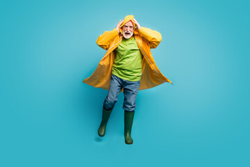 Full length photo of rushing home grandpa walk run street puddles rainy weather slippery wet road wear jeans jumper gum boots yellow raincoat isolated blue color background