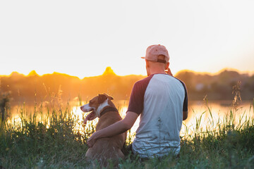 Man hugs his dog in sunset by the lake. Pets and human friendship, taking care, spending time...