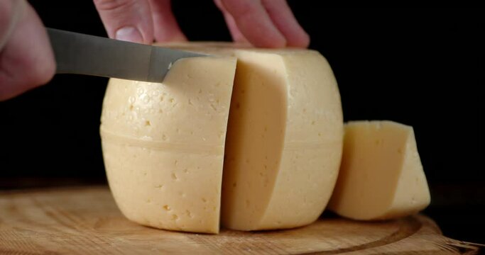 Male hand cut off a piece of cheese on a cutting Board.