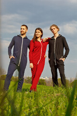 Two guys and a girl have a rest in the park on the nature. Dressed in tracksuits. Healthy lifestyle. Emotions, joy, fun, happiness, friendship.