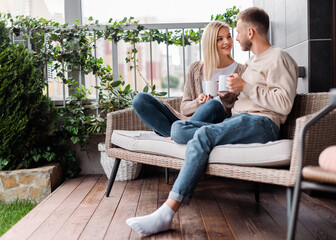 Obraz premium Happy woman and man looking at each other and holding cups while sitting on outdoor sofa
