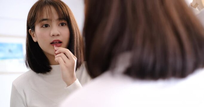 Asian woman make up with cosmatic applying lipstick front mirror at home