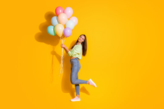 Full size profile photo of pretty lady good mood hold many air balloons party guest surprise wear green cropped sweatshirt jeans shoes isolated vivid bright yellow color background