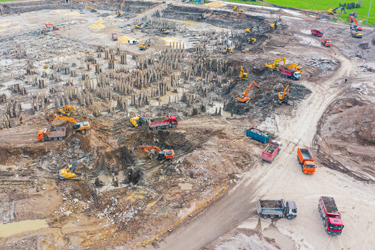 Working excavators on the site of a demolished building. Loading cement residues into the crushing equipment and trucking soil, aerial top view of the demolished building and pit with piles.