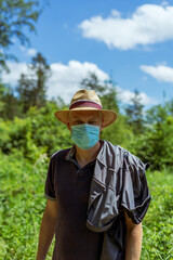 Mann über 40 mit einem Mundschutz und einem Sonnenhut im Wald, Natur, Sträucher, Corona, Selbstschutz