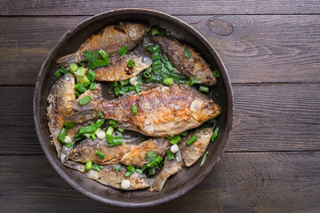 Frying pan with tasty crucian carp on wooden background 