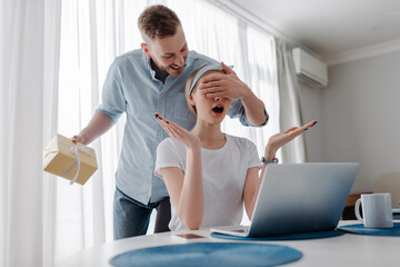 Fototapeta premium handsome man covering eyes of surprised girlfriend while holding present