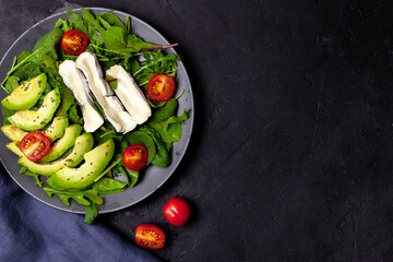 Fresh salad with spinach, avocado, tomatoes and cheese on black background, flat lay.