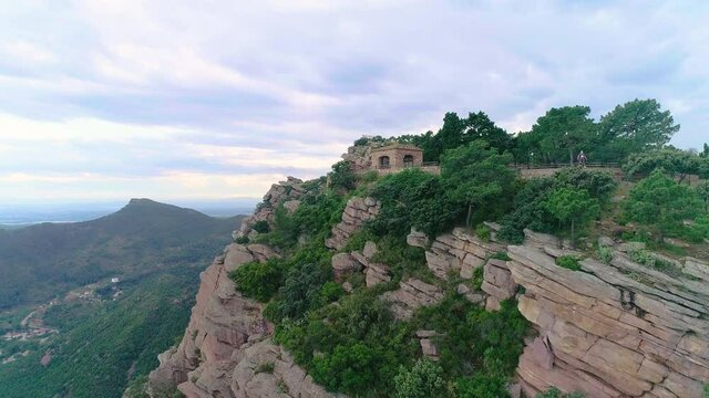 monta&ntilde;a rocosa de gran profundidad y ermita en la cima con hombre con mascarilla en vuelo r&aacute;pido de dron acerc&aacute;ndose 