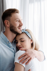 happy man hugging cheerful girlfriend at home