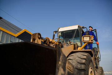 Builder is sitting in the bulldozer cabin and looking to the site