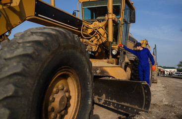 young man contractor builder in blue overalls is looking to the bulldozer wheel.