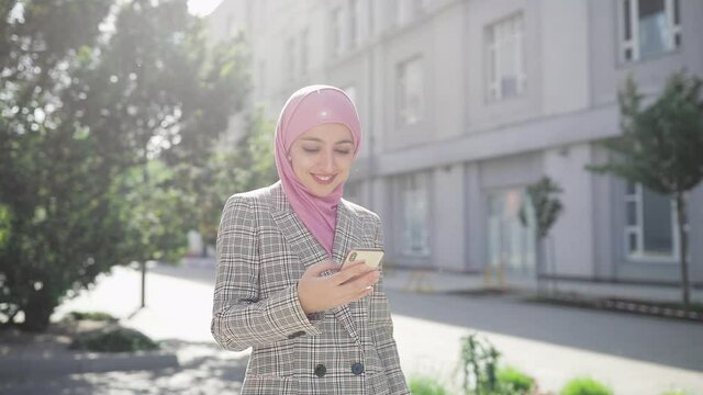 Young beautiful muslim woman wearing hijab headscarf walking in the city using smartphone. Communication, online shopping, social network concept.