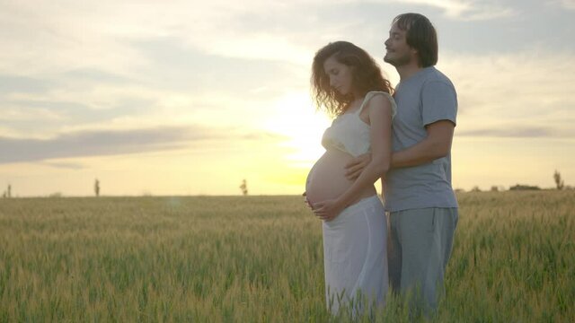 Pregnant couple of husband and wife feels love and relax at home. Young expecting woman holds baby in pregnant belly. Father take care of pregnant mother. Concept of maternity and pregnancy care.
