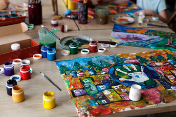 A bright watercolor drawing lies on a table next to cans with multi-colored paint and brushes. Art Studio.