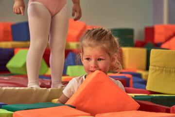 A girl gymnast plays in a multi-colored gymnastic sponge cube. Colorful baby cubes. Soft for...