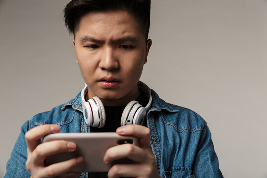 Image of focused young asian man playing video game on smartphone