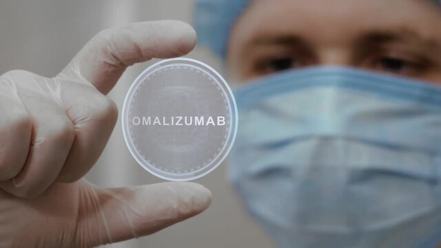 Doctor looks at innovative holographic projection with text Omalizumab. Male scientist in medical mask conducting technological research on hologram. Concept of futuristic medicine, device of future