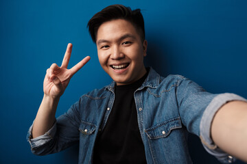 Image of asian man gesturing peace sign and taking selfie photo