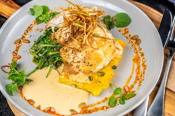 A serve of grilled Barramundi fish with Paella Risotto cake, presented on a round plate