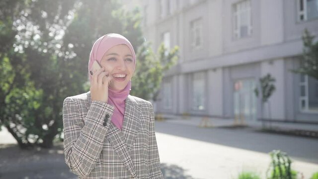 Young beautiful muslim woman wearing hijab headscarf walking in the city talking with someone by smartphone. Communication, online shopping, social network concept.