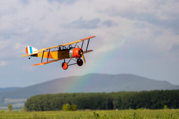 R/C biplane airplane landing on the grass with beautiful rainbow in the background