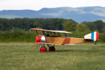 Obraz na płótnie Canvas R/C biplane airplane landed on the grass with one wheel above the ground