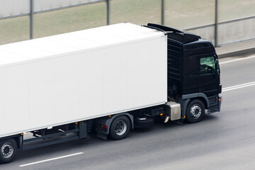 Truck with a black cab and a white trailer compartment drives on the highway.