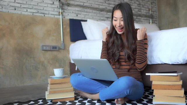 While working on her laptop, a young woman reacts with joy as she sees her success on screen.  