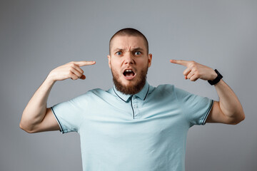 Portrait of a young man in a blue t-shirt angry shouting over a gray background. isolated.