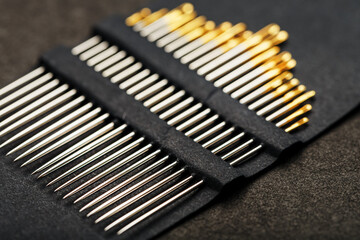 Gold sewing needles on a black background in a row.