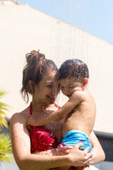 Mother holding a child in a swimsuit as they smile and water falls on them