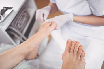 Pedicurist doing professional medical pedicure procedure in beauty salon with special eguipment. Foot treatment in SPA salon. Podiatry clinic. Beautician doctor hands in white gloves with female legs