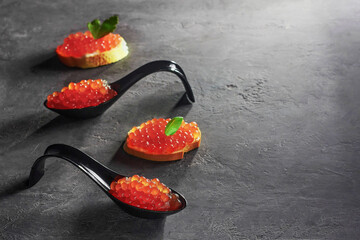 Sandwiches and black spoons with red caviar.