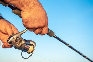 Men's hands holding a fishing rod and twist the handle of the fishing reel. Shallow depth of field, soft focus