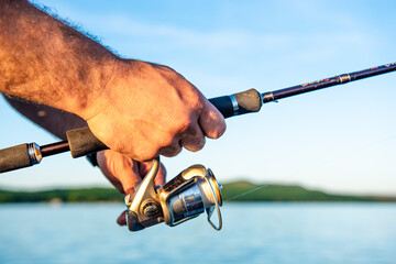 Men's hands holding a fishing rod and twist the handle of the fishing reel. Shallow depth of field, soft focus