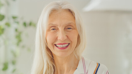 Authentic Beauty Portrait Shot of Senior Female Pensioner in a Bright Room at Home. Beautiful Old Female with Gray Hair Poses for the Camera and Gently Smiles. Happy Elderly Person Full of Health.