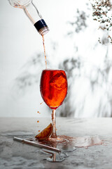 Refreshing aperol spritz cocktail with straw and sliced orange on a grey background- summer day sunlight shadows