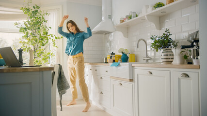 Attractive Young Female in Jeans Shirt and Brown Pants is Creatively Dancing in the Kitchen. Sunny Modern Kitchen with Healthy Lifestyle Vibes. Happy Beautiful Girl Relaxing at Home.