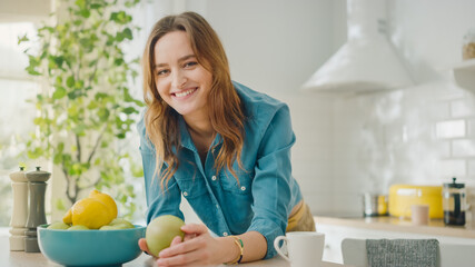 Authentic Beauty Portrait of a Beautiful Brunette Female Holding a Big Green Apple in a Bright Room at Home. Pretty Young Woman Poses for the Camera and Gently Smiles. Healthy Natural Vegetarian.
