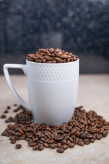 a white cup filled with roasted cinnamon coffee beans standing on brown marble surrounded by coffee beans