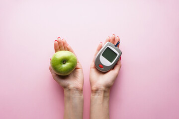Digital glucometer and fruit in the hands of a woman on a pink background, flat lay. Diabetes concept.