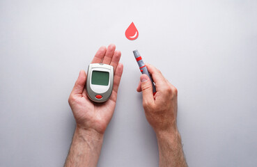 Glucometer, lancet pen in male hands on a gray background with a drop of blood, flat lay. Diabetes concept. World Diabetes Day, November 14th.