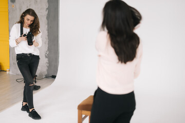 Woman photographer and female model together looking at made photo and talking,smiling, white background. Concept of creative work in photo studio, backstage job.