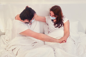 Couple fights in medical masks while lying in bed, domestic violence in quarantine while isolated from coronavirus