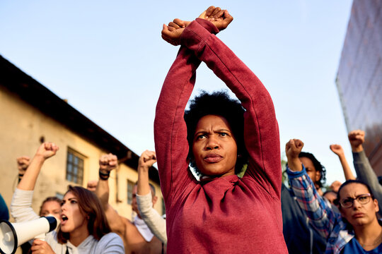 Black woman with clenched fists above her head protesting with group of people on the streets.