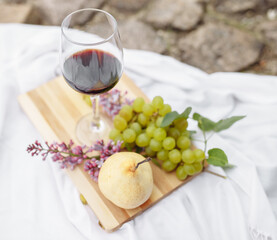Picnic in the nature in the park. A glass of wine green grapes yellow pear red apple lilac on a...