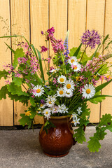 Colorful meadow flower bouquet in a clay mug on a natural background on a sunny day. Summer solstice bouquet in Latvia, Baltics.